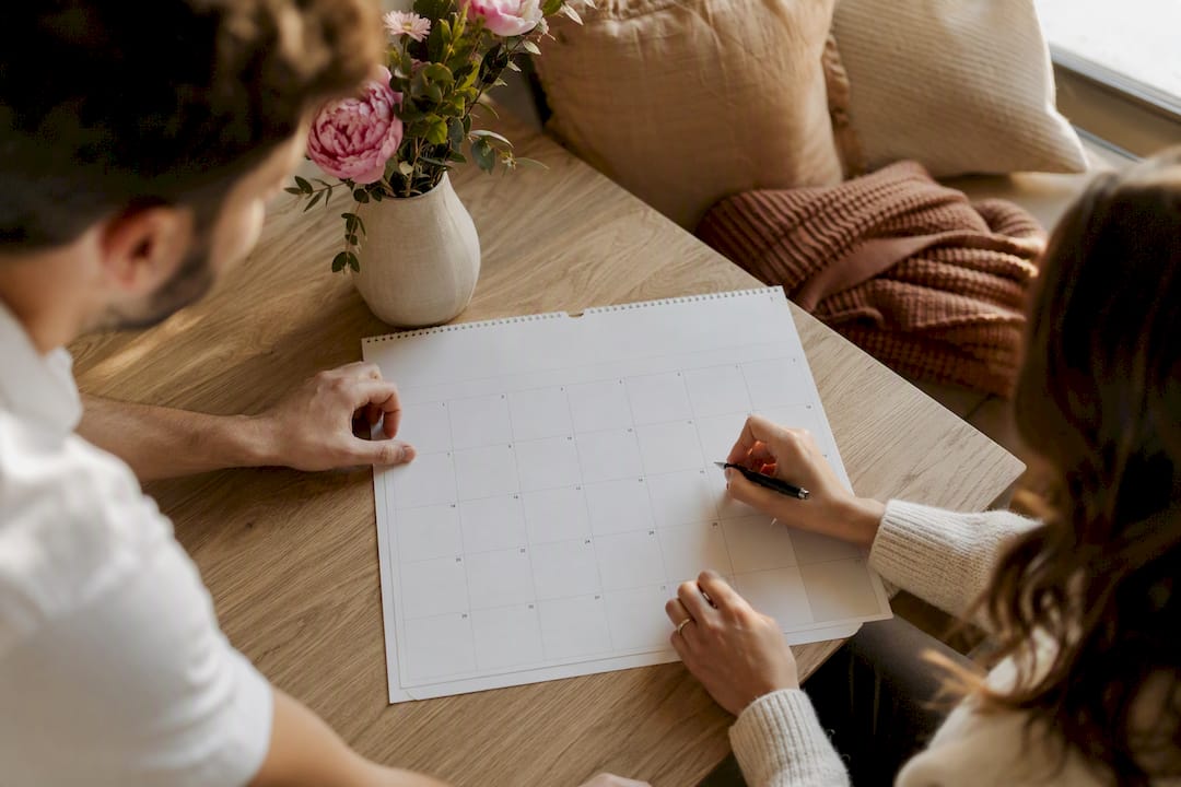 Mains marquant une date sur un calendrier avec des fleurs à côté